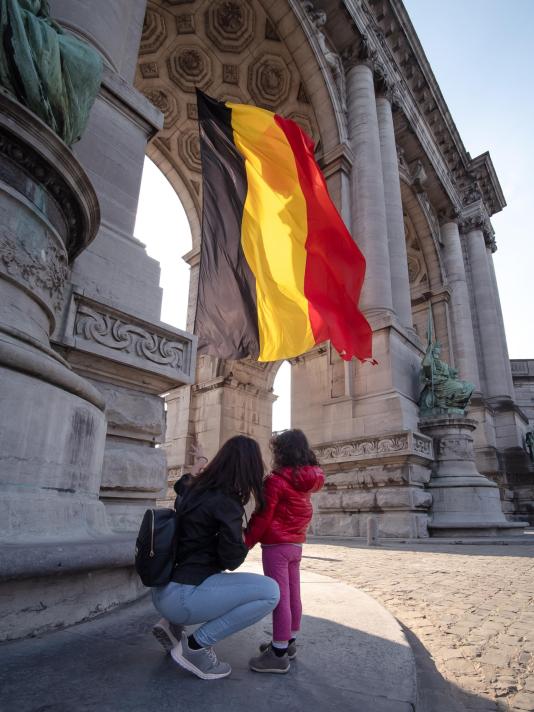 Mother and child looking at a Belgian flag with monument in the background