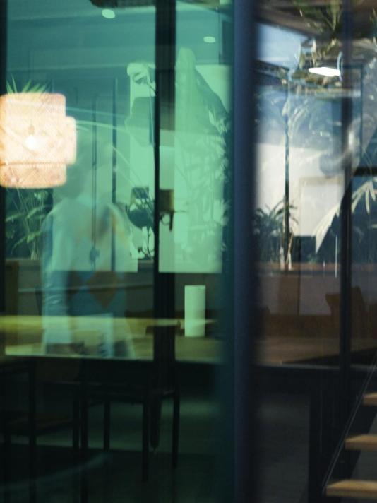 A woman gracefully walks through an office, her silhouette reflected in the glass wall, creating a captivating visual as she navigates the professional environment.
